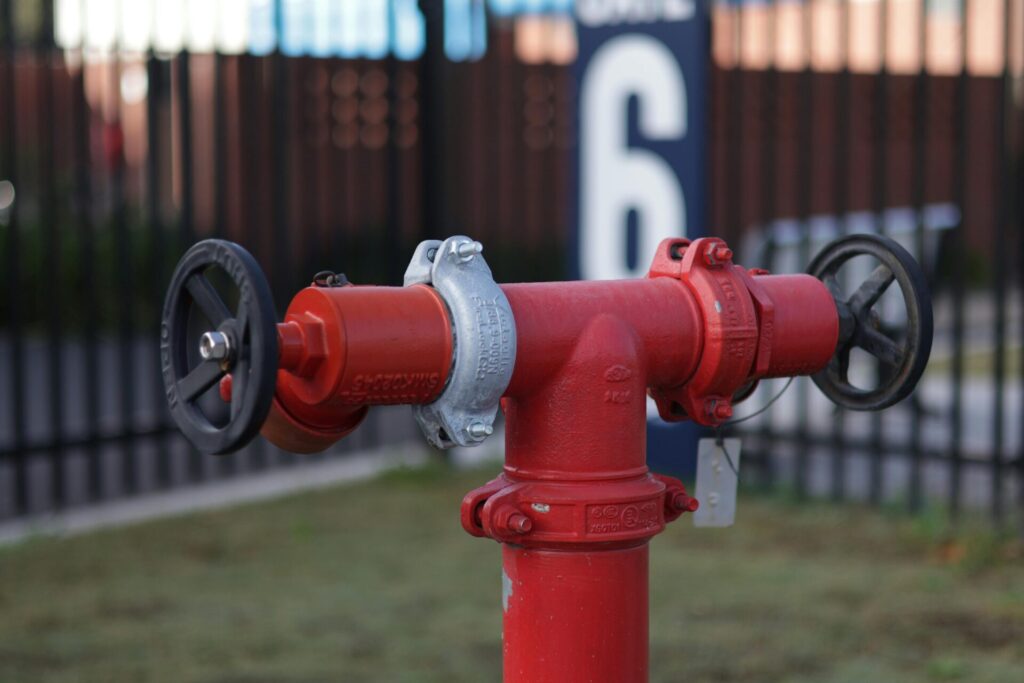 Montaje técnico de hidrante de columna roja con doble salida y volantes de apertura para redes de hidrantes en entorno industrial.